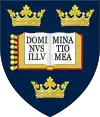 A shield displaying a coat of arms; on a dark blue background, an open book displays the words "Dominus illuminatio mea", with two gold crowns above and one below